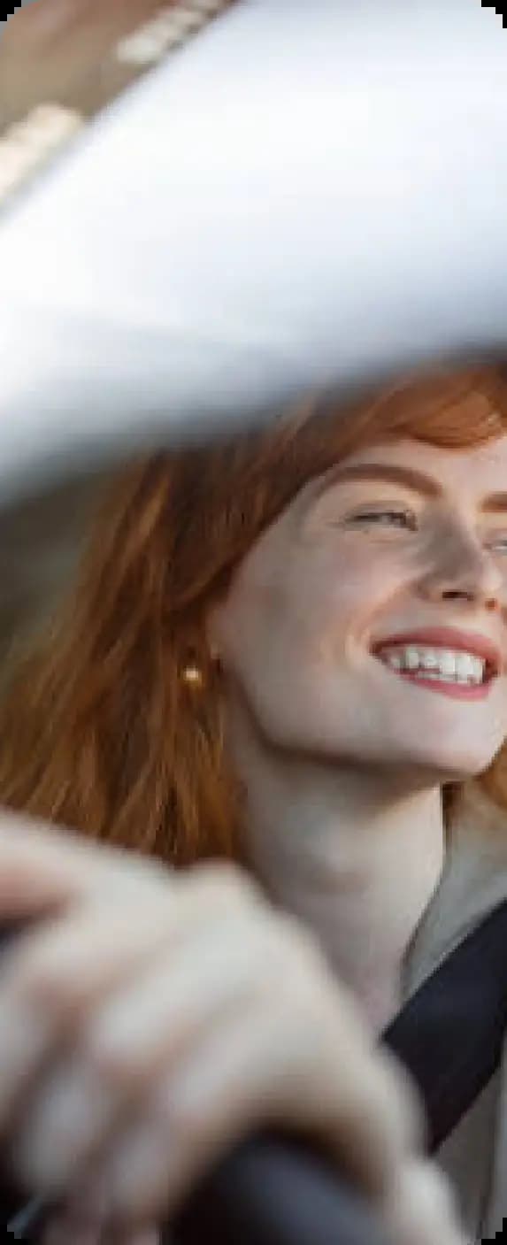 Person with red hair smiling while driving car in daylight